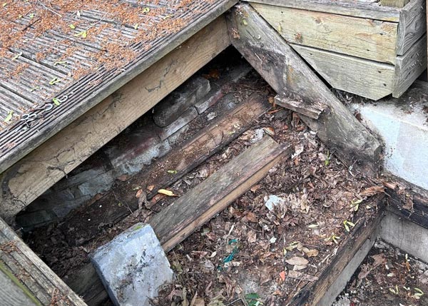 damaged wooden structure with dirt and debris revealing hidden area and signs of decay in need of repair