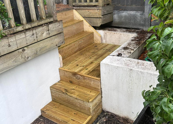 wooden stairs leading to a garden area featuring two steps and surrounding greenery