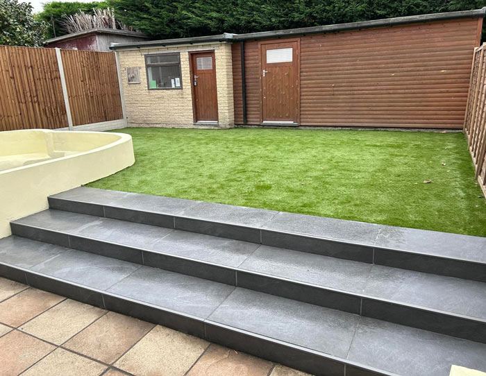steps leading to a green lawn with a small round seating area and two wooden storage sheds in the background outdoor space design ideas 3 elements